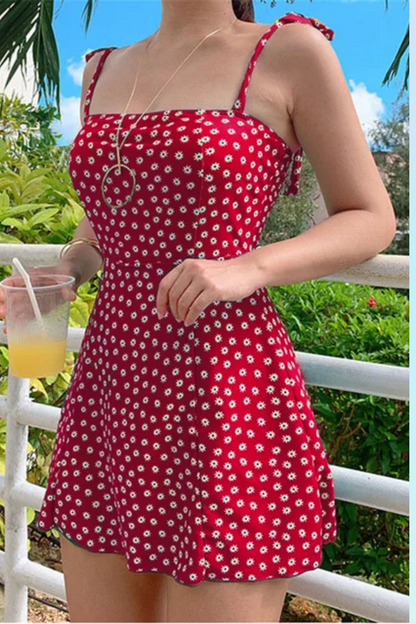 Une personne dans un Maillot de Bain Rouge Femme | Robe 1 pièce de BREEZEBEEZ avec imprimé floral blanc tenant un verre de limonade en plein air par une journée ensoleillée.