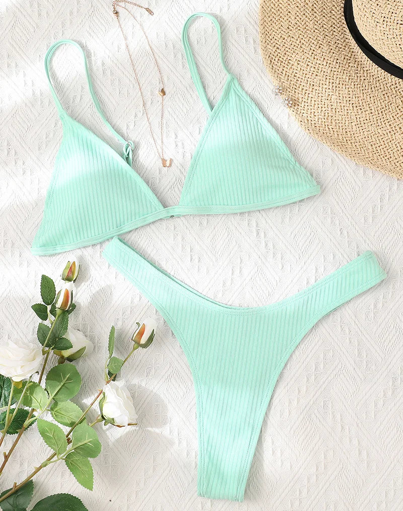 Un Maillot de Bain Vert 2 Pièces Bikini 2024 Sexy by BREEZE BEEZ unique et côtelé vert menthe, disposé à plat à côté d'un chapeau de paille et d'un brin de roses, suggérant un look élégant et rafraîchissant pour profiter des vacances.