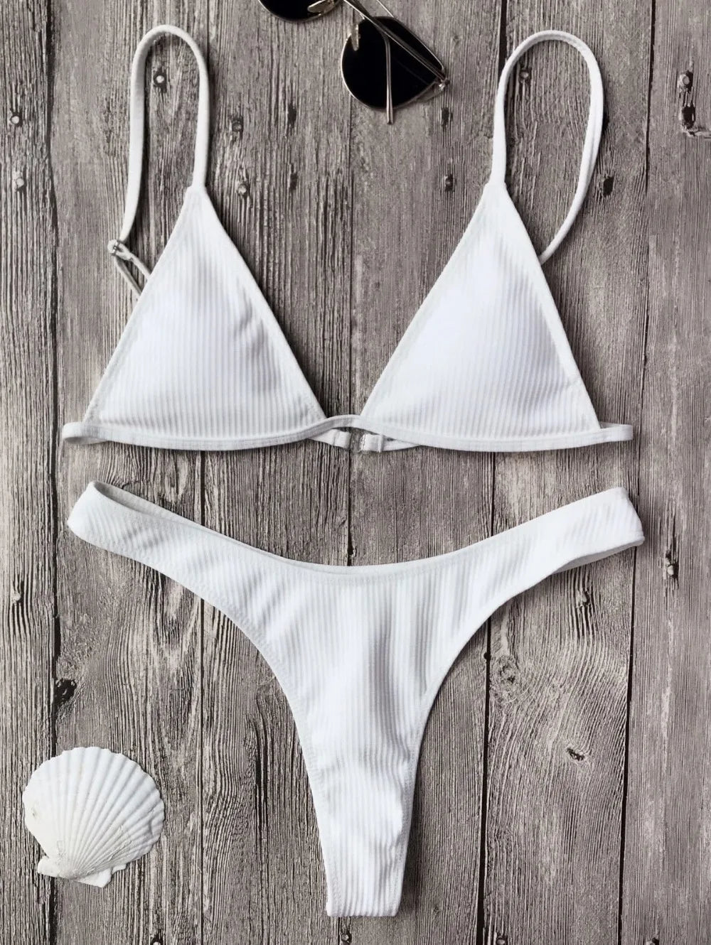 White Maillot de Bain Femme 2 Pièces Bikini 2024 Maillot de bain sexy disposé sur une surface en bois, accompagné d'une paire de lunettes de soleil et d'un coquillage, évoquant un thème prêt à la plage au soleil par BREEZE BEEZ.