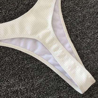 Un gros plan d'un Maillot de Bain Femme 2 Pièces Bikini 2024 Sexy blanc disposé sur une surface grise texturée, évoquant l'ambiance sereine du soleil à la plage par BREEZE BEEZ.