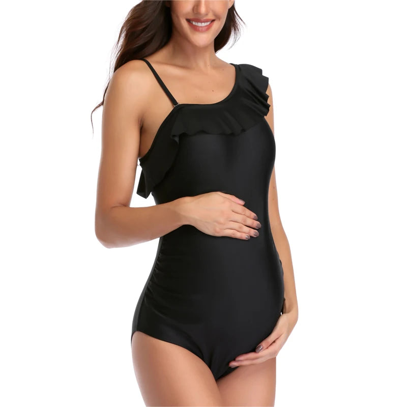 Une femme posant dans un BREEZE BEEZ Maillot de Bain Femme Enceinte | Noir 1 Pièce avec détails volants sur l'épaule.