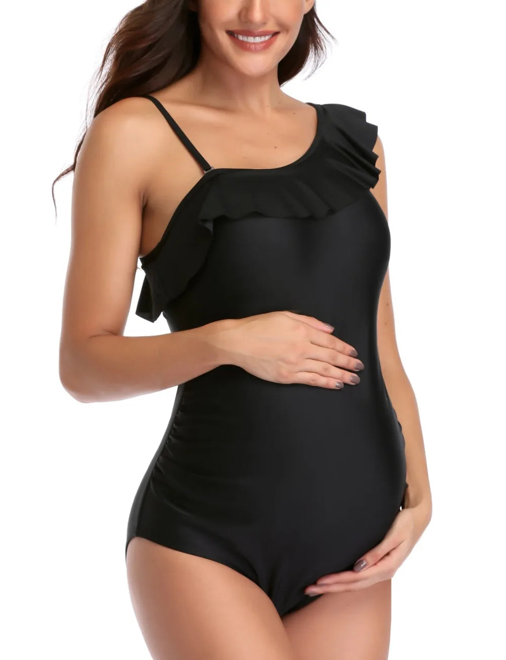 Une femme souriante présentant un maillot de bain noir Maillot de Bain Femme Enceinte asymétrique avec un très beau détail de volants, berçant doucement son baby bump. Marque : BREEZEBEEZ