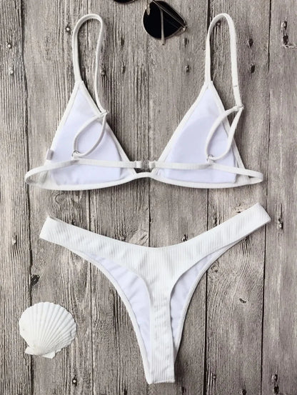 Un maillot de bain sexy blanc Maillot de Bain Femme 2 Pièces Bikini 2024 disposé sur un fond en bois rustique à côté d'une paire de lunettes de soleil, le sable et un coquillage, évoquant une ambiance de plage estivale balnéaire.