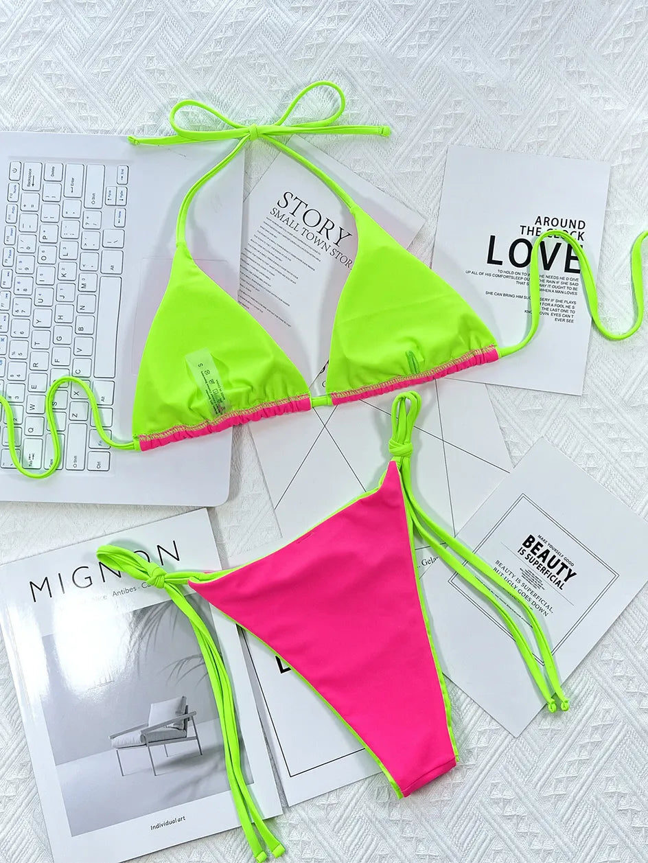 Un bikini BREEZE BEEZ Maillot de Bain Femme 2 Pièces vert fluo et rose vif disposé sur un fond texturé blanc, flanqué de magazines chics et d'un clavier blanc élégant, suggérant un mélange de travail, de mode et de détente.