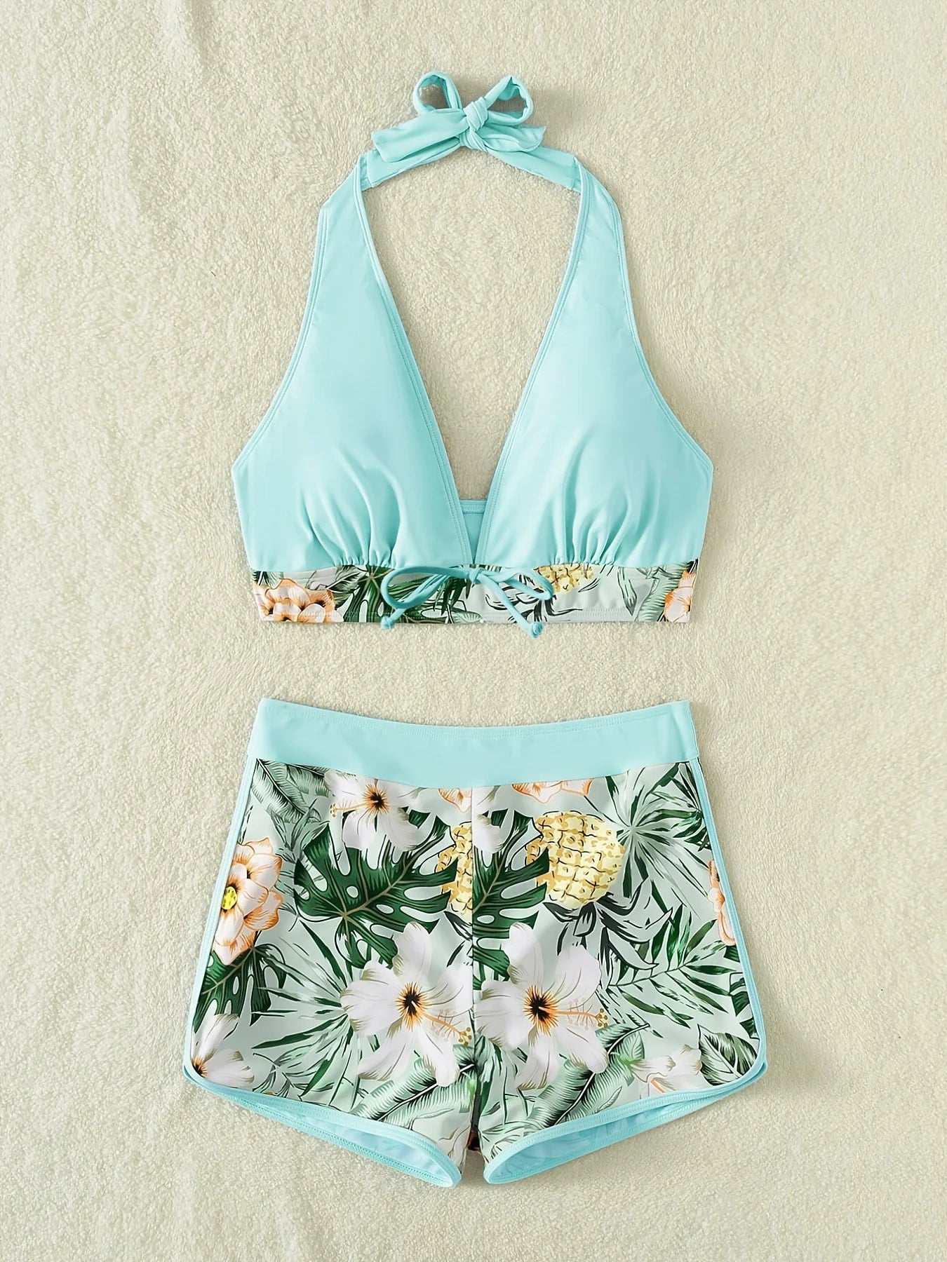 Un maillot de bain haut dos nu bleu clair avec un bas à imprimé floral posé à plat sur une surface de couleur crème, parfait pour une fête de la mer par BREEZE BEEZ.