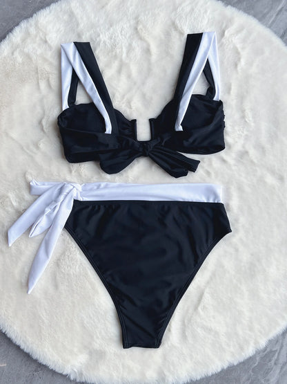 Nos Maillots Bain Bandeau 2 Pièces Noir, conçus pour toutes les morphologies, présentent un bikini noir avec liseré blanc et des accents de nœuds, posé sur un fond blanc de la marque BREEZE BEEZ.