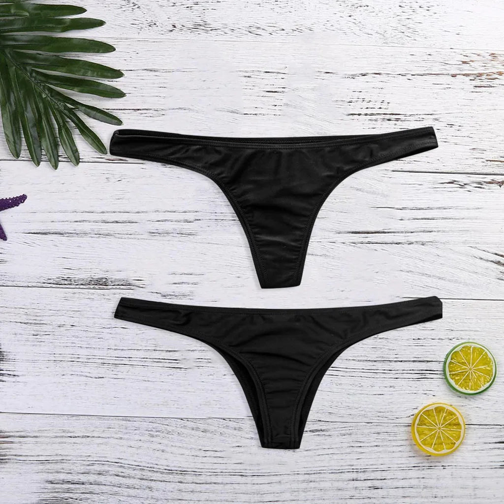 Bas Maillot de Bain Femme | 1 Pièce Noir de BREEZE BEEZ, conçue pour toutes les morphologies, est disposée sur une surface en bois blanc, flanquée de feuilles tropicales vertes et de tranches de citron vert, créant un thème beachwear estival.