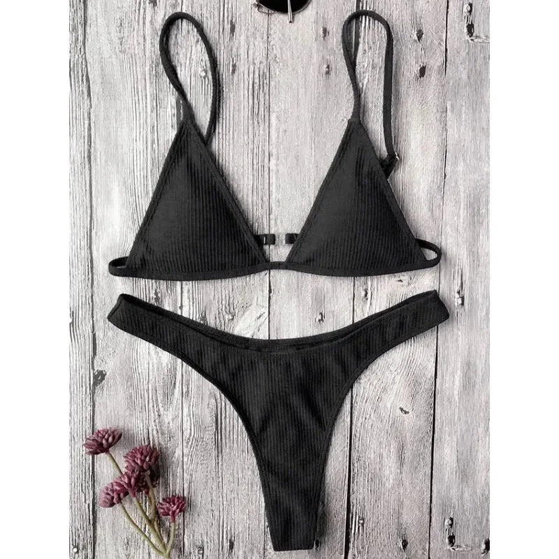 A Maillot de Bain 2 Pièces Noir Bikini 2024 Ensemble sexy composé d'un haut triangle et d'un bas assorti, affiché sur un fond en bois rustique, accompagné d'un petit bouquet de fleurs roses sur le côté. Conçues pour toutes les morphologies par BREEZE BEEZ.