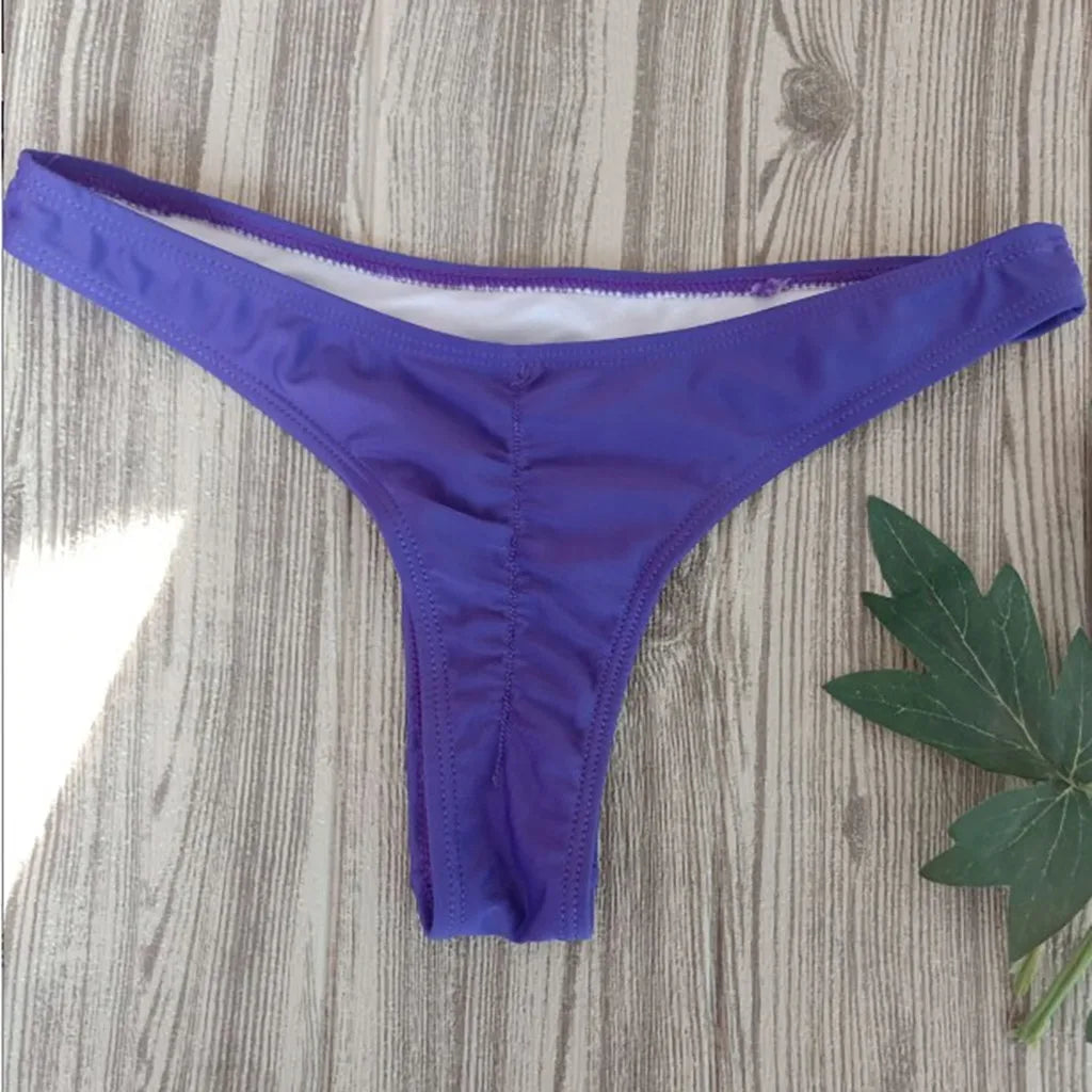 Bas Maillot de Bain Femme 1 Pièce Violet de BREEZE BEEZ affiché sur une surface en bois avec une feuille verte sur le côté, l'oasis des femmes qui cherchent le maillot de bain parfait.