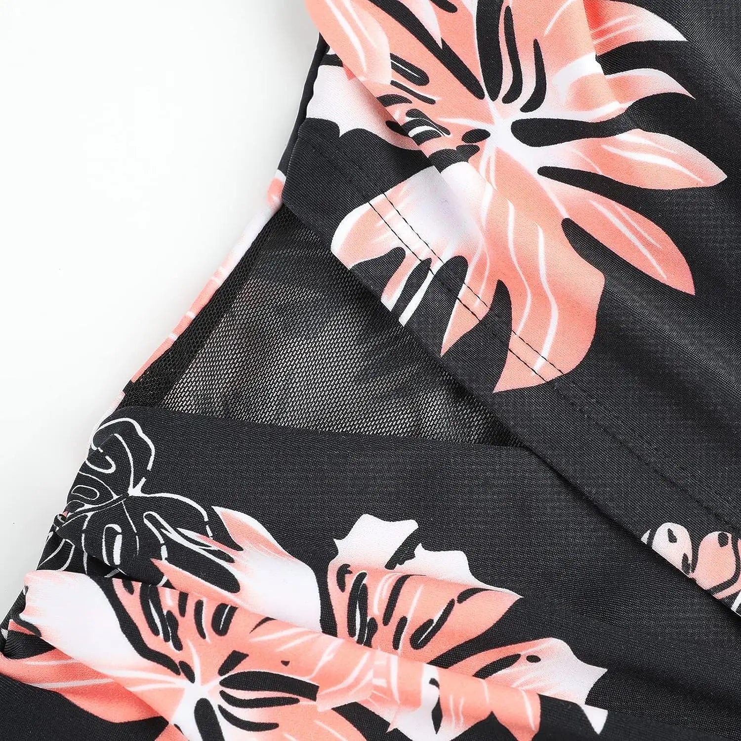 Un gros plan d'un BREEZE BEEZ Maillot de Bain Femme 1 Pièce Elégant Floral, avec un motif floral tropical rose et blanc, avec des détails délicats en forme de maille, parfait pour un cadre balnéaire.