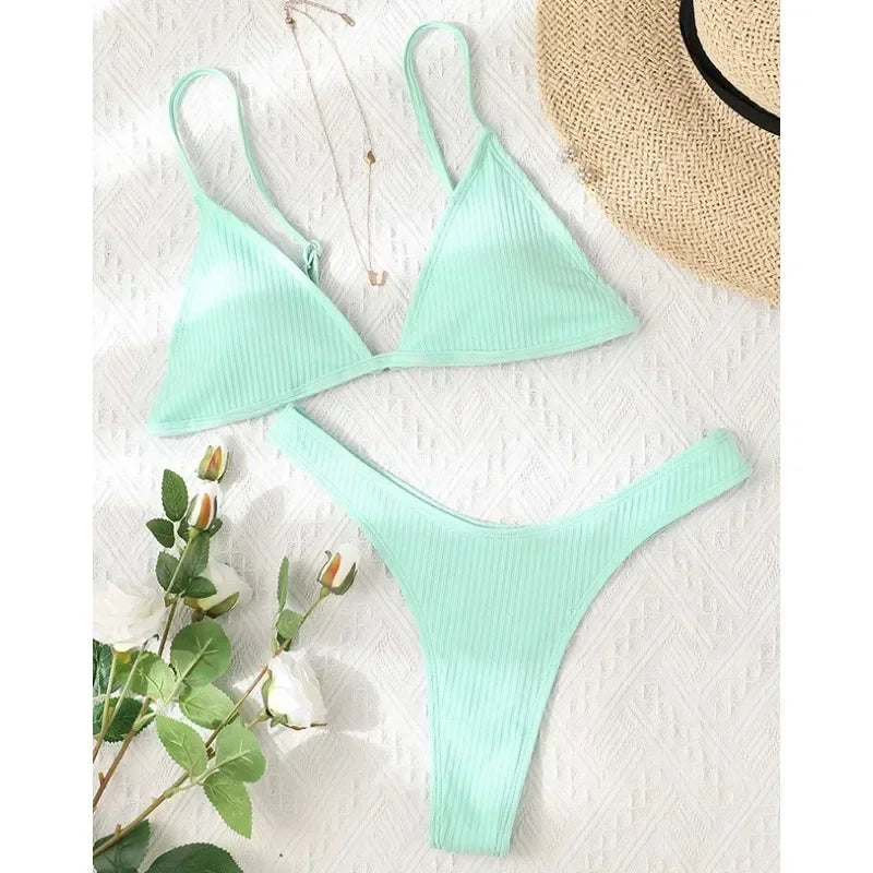 Un confortable ensemble sexy BREEZE BEEZ Maillot de Bain Vert 2 Pièces Bikini 2024 soigneusement disposé sur une surface blanche texturée, accompagné d'un brin de roses blanches et d'un chapeau de paille partiellement visible dans le coin supérieur, évoquant un sentiment de