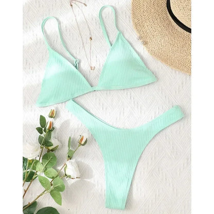 Un confortable ensemble sexy BREEZE BEEZ Maillot de Bain Vert 2 Pièces Bikini 2024 soigneusement disposé sur une surface blanche texturée, accompagné d'un brin de roses blanches et d'un chapeau de paille partiellement visible dans le coin supérieur, évoquant un sentiment de