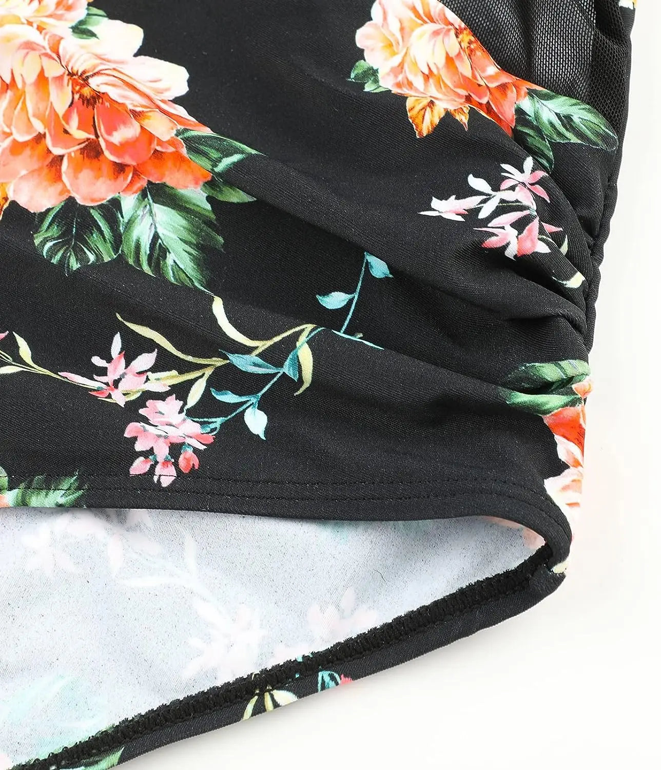 Gros plan d'un morceau de tissu noir avec un imprimé floral vibrant, mettant en vedette des fleurs orange et roses avec un feuillage vert, avec un détail en maille transparente et une couture froncée extensible. À la plage, ce BREEZE BEEZ Maillot de Bain Femme 1 Pièce Elégant Floral.