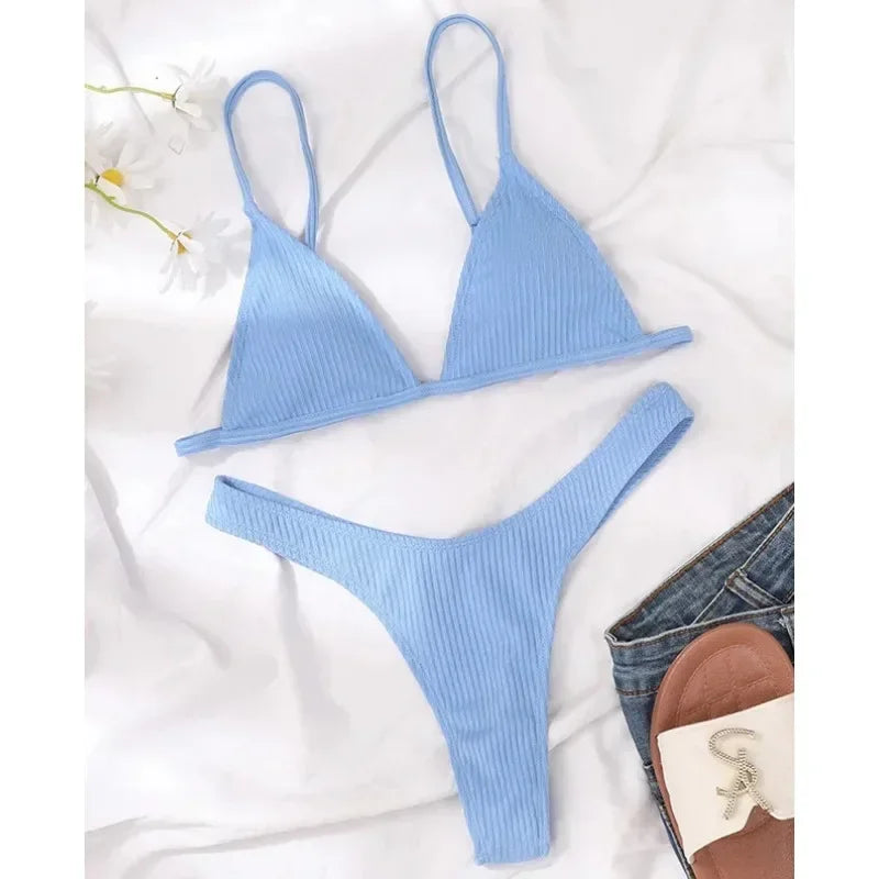 Un Maillot de Bain Femme 2 Pièces Bikini 2024 Sexy bleu clair de BREEZE BEEZ disposé sur une surface blanche, accompagné d'une paire de jeans et de sandales, évoquant une ambiance balnéaire décontractée.