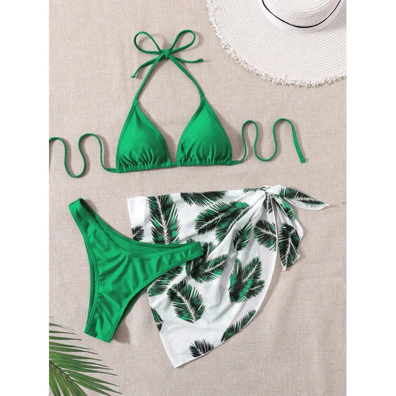 Maillot de bain tropical : un très beau haut de bikini BREEZE BEEZ vert vif associé à un bas de style paréo à imprimé feuilles de palmier, ainsi qu'un chapeau de soleil chic, signalant une préparation élégante pour une journée ensoleillée à la plage.