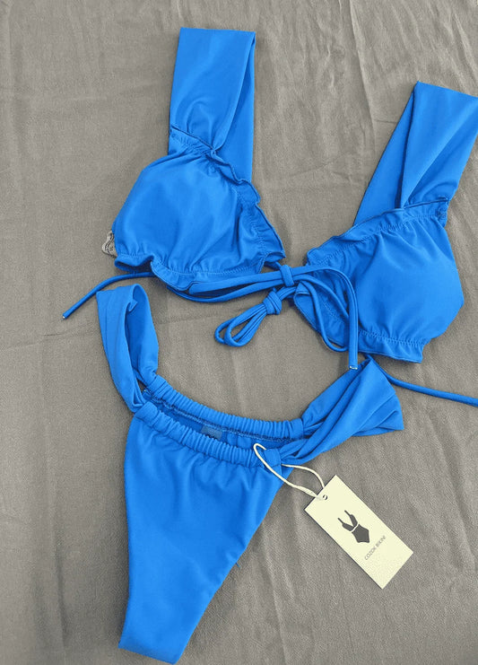 Bienvenue dans notre boutique en ligne, découvrez un nouveau Maillot de Bain 2 Pièces Bleu Bikini BREEZE BEEZ avec étiquettes, posées sur une surface de tissu gris, attendant son premier jour à la plage.