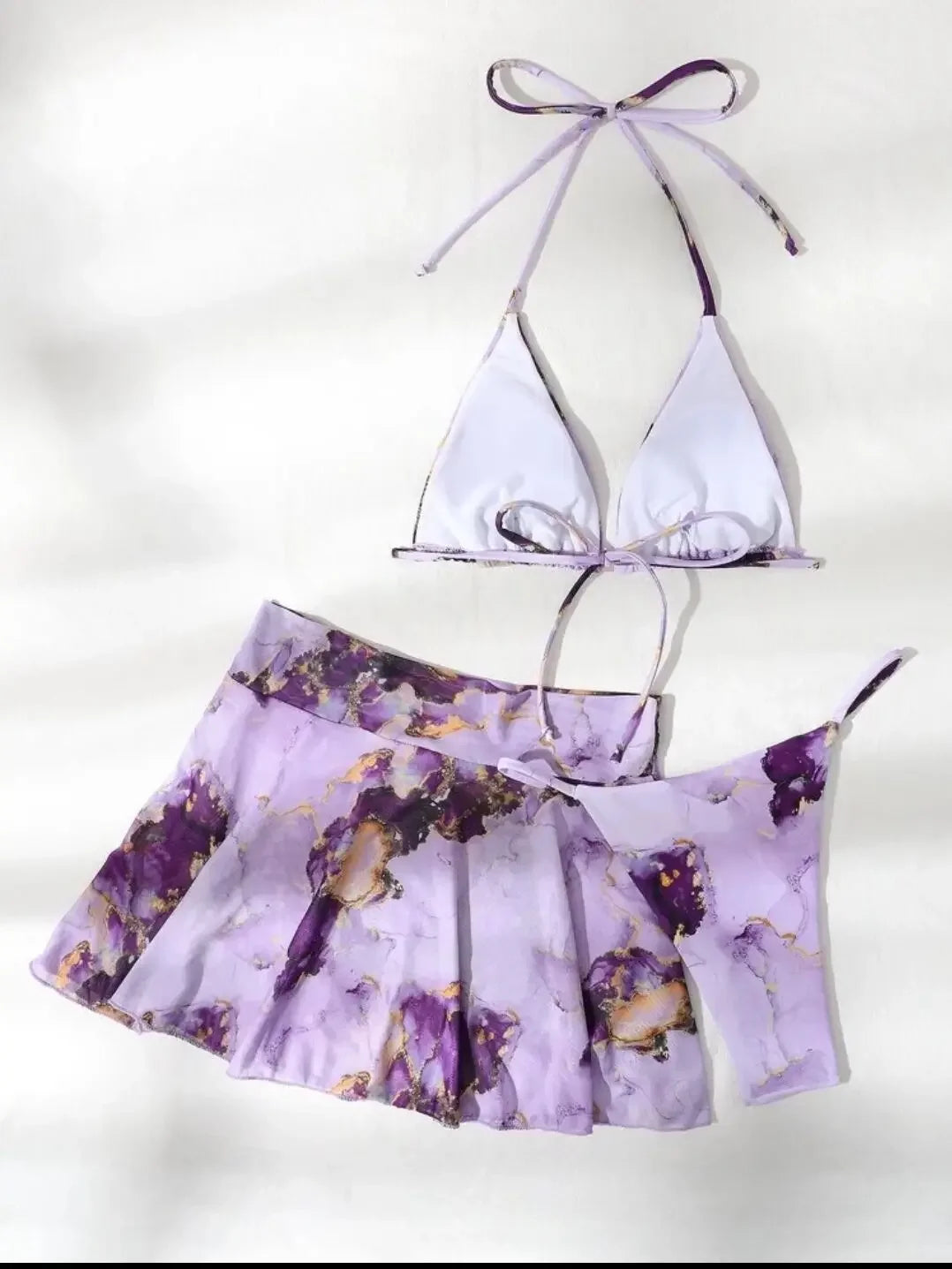 Un maillot de bain jupette pour femme BREEZEBEEZ à motif floral lilas associé à un haut sexy 3 pièces Mauve assorti avec des détails violets sur fond blanc.