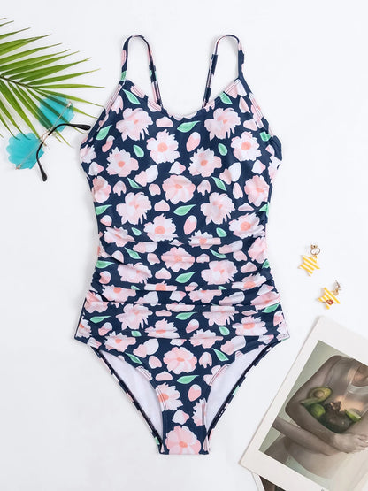 Maillot de bain Floral Maillot de Bain Femme 1 Pièce Dos Croisé de BREEZE BEEZ disposé sur une surface blanche, accessoirisé d'une feuille de palmier verte, de lunettes de soleil et de boucles d'oreilles élégantes, prêt pour une journée ensoleillée à la plage.