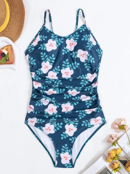 Un Maillot de Bain Vert 1 Pièce Croisé à motifs floraux de BREEZE BEEZ unique affiché à plat sur une surface blanche, accompagné d'accessoires d'été comme un chapeau de paille et des fleurs décoratives, évoquant une ambiance venteuse et prête pour la plage.