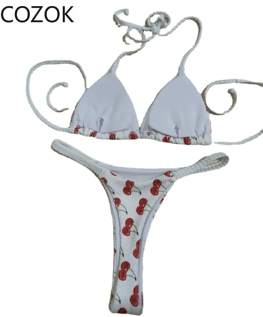 Une description: Un Maillot de Bain Blanc Femme 2 Pièces Bikini à motif de cerises, conçu pour toutes les morphologies, suspendu devant un fond neutre par BREEZE BEEZ.