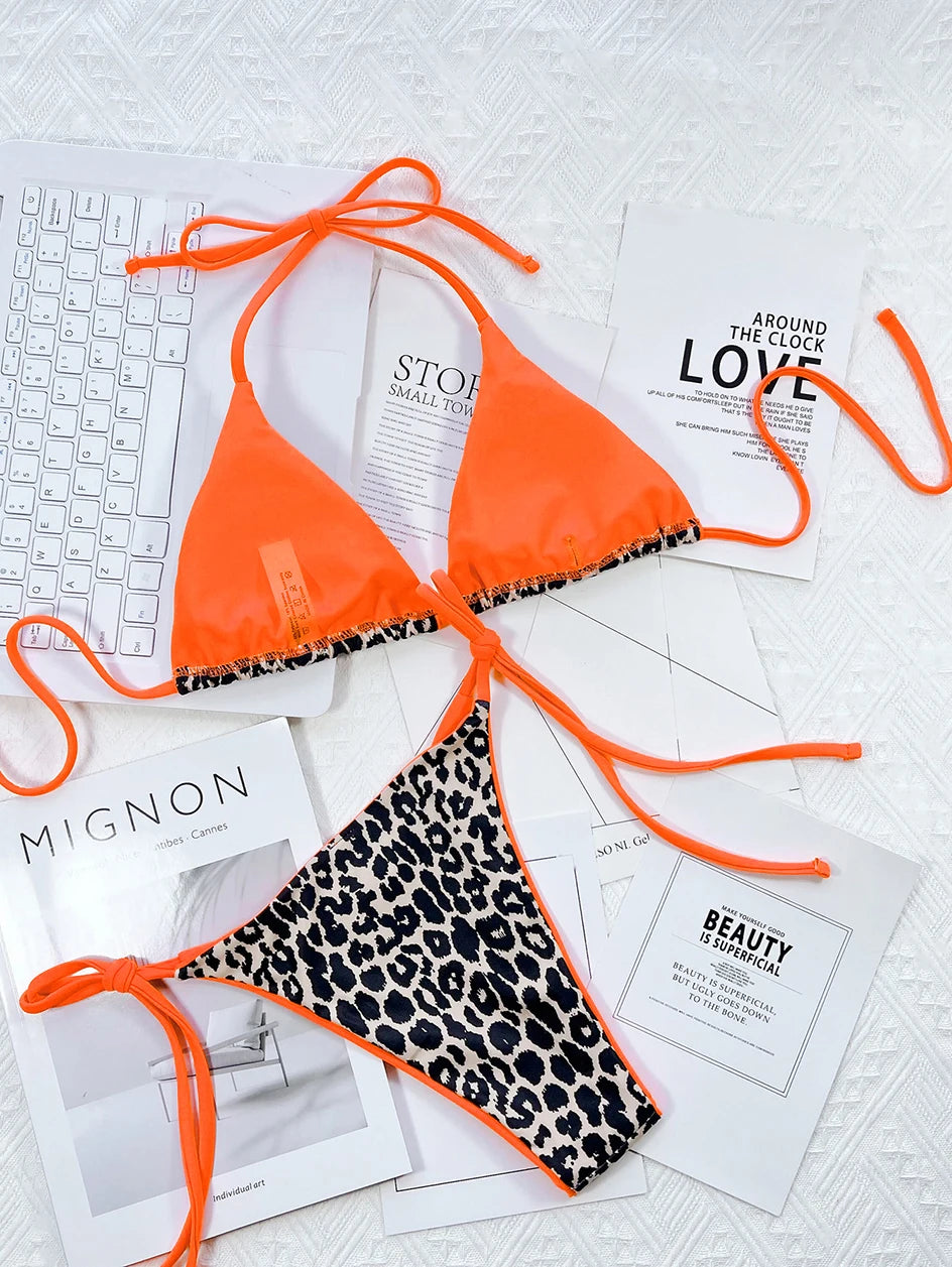 Un bikini Maillot de Bain Femme 2 Pièces imprimé orange vif et léopard de BREEZE BEEZ est disposé sur un fond balnéaire avec des magazines de mode et un clavier, suggérant un mélange de travail, de style et de loisirs.