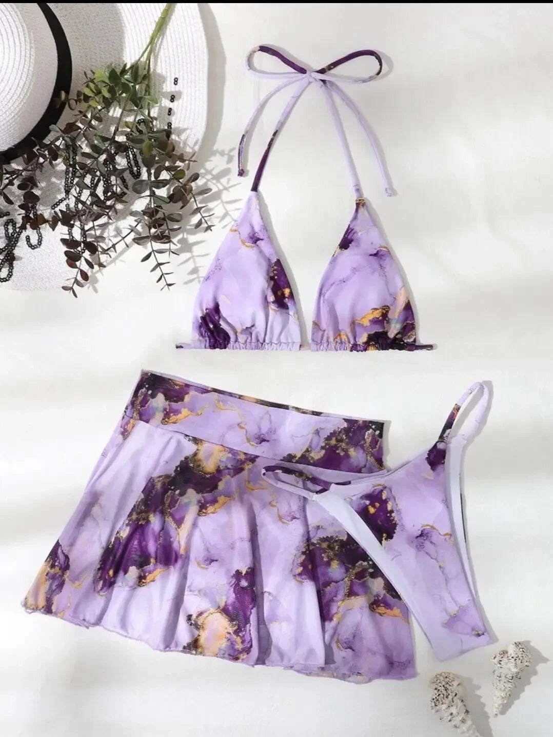 Un Maillot de Bain Jupette | Mauve 3 pièces Sexy élégant avec une jupette pour femme assortie, disposé avec élégance à côté d'un chapeau de BREEZEBEEZ.