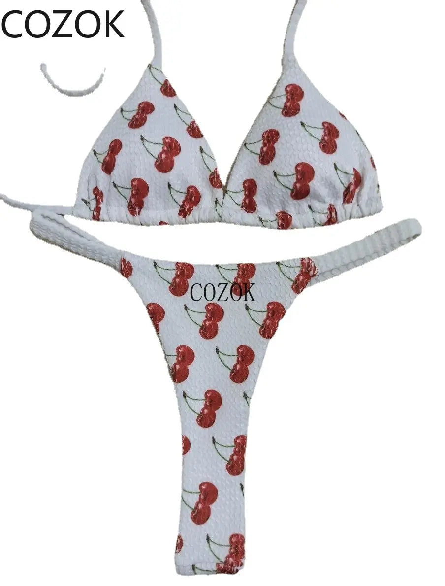 Un Maillot de Bain Blanc Femme 2 Pièces Bikini avec un motif de cerises, conçu pour toutes les morphologies, affiché contre un fond uni par BREEZE BEEZ.