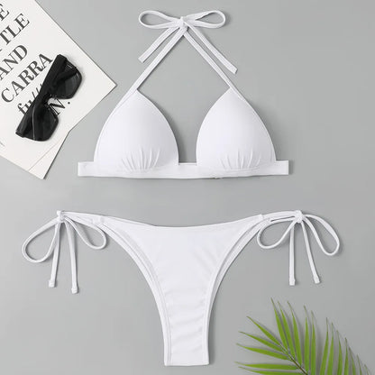 Un maillot de bain Maillot de Bain Blanc 2 Pièces de BREEZE BEEZ posé à plat, comprenant un haut dos nu avec des cordons à nouer et un bas assorti avec des liens latéraux, accompagné de lunettes de soleil noires et d'une feuille de plante verte, le tout sur un fond neutre.