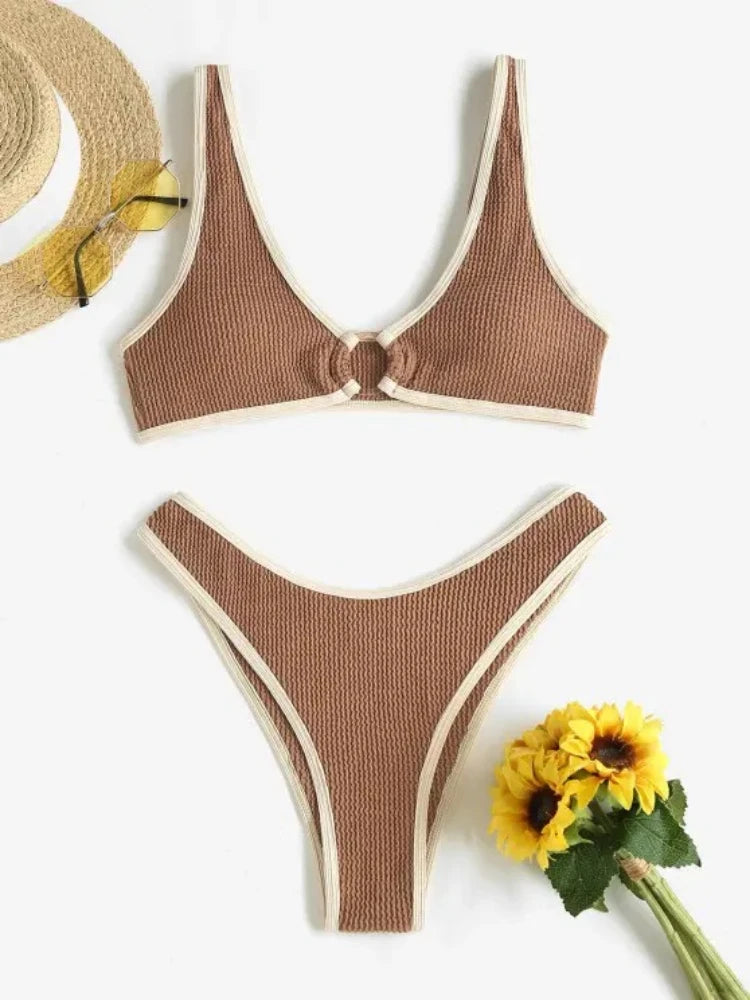 Un élégant Maillot de Bain Femme 2 Pièces Marron côtelé et noué sur le devant par BREEZE BEEZ dans des tons terre, associé à un chapeau de paille et des lunettes de soleil, aux côtés d'un bouquet de fleurs jaunes, suggérant un "au soleil" chaud et estival.