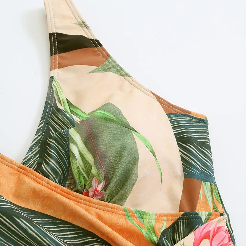 Un gros plan d'une feuille tropicale et d'un imprimé floral sur un segment d'un maillot de bain avec une combinaison de couleurs vertes, beiges et roses sur un fond uni, mettant en valeur le BREEZE BEEZ Maillot de Bain 2 Pièces Imprimé.