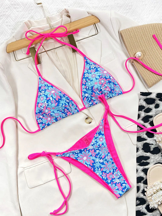 Un Maillot de Bain Femme 2 Pièces Bikini Floral bleu vif avec des accents roses disposés sur un blazer blanc chic, accompagné d'accessoires élégants dont une pochette en paille et des sandales ornées de perles, prêt pour une journée à la mer par BREEZE BEEZ.