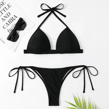 Une pose à plat d'un élégant ensemble Maillot de Bain 2 Pièces Noir de BREEZE BEEZ, conçu pour toutes les morphologies, avec des détails à nouer, accompagné de lunettes de soleil, d'une plante décorative et d'un magazine, soigneusement disposés pour un.