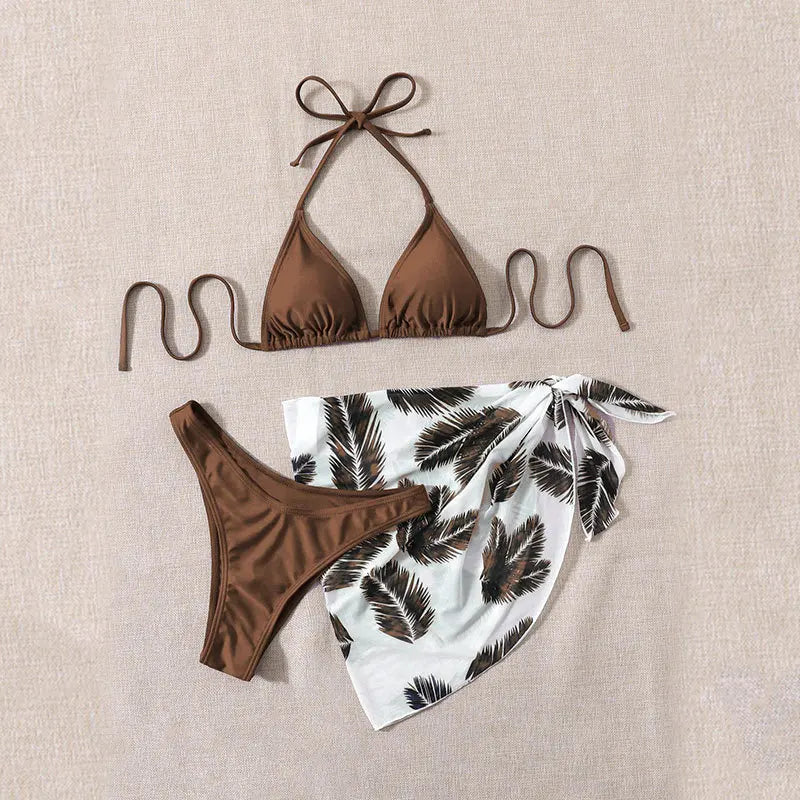 A élégant BREEZE BEEZ Maillot de Bain Femme 3 Pièces | Ensemble haut & Bas composé d'un haut marron et d'un bas échancré orné d'un imprimé de feuilles tropicales blanches et noires, soigneusement disposés sur un fond texturé beige, prêt pour une journée à la plage.