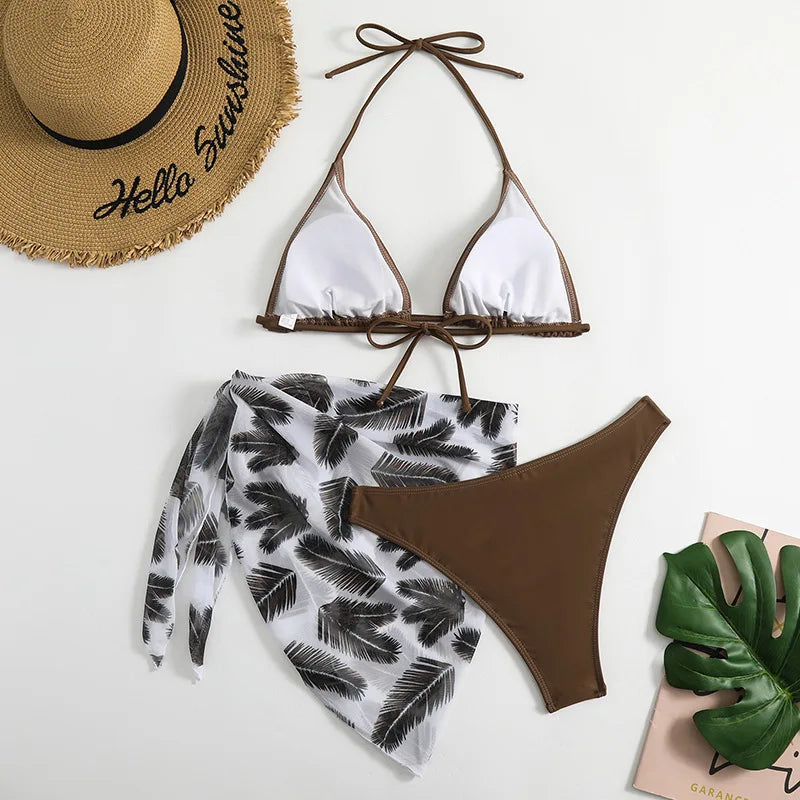 Les essentiels de l'été : un ensemble tendance blanc et marron BREEZE BEEZ Maillot de Bain Femme 3 Pièces associé à un élégant chapeau de paille, sur un fond avec un accent de feuilles tropicales pour une ambiance parfaite pour une escapade à la plage.