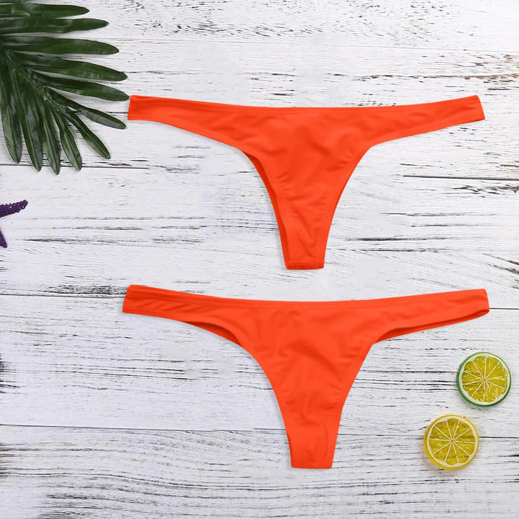 Deux bas de bikini orange BREEZE BEEZ soigneusement disposés sur une surface en bois avec des accents tropicaux dont une feuille de palmier et des tranches de citron vert, suggérant un thème estival et prêt pour la plage. Bienvenue dans notre boutique en ligne, nos bas maillot de bain femme Orange 1 Pièce.