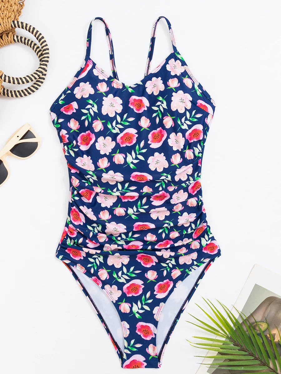 Une élégante pièce florale Maillot de Bain Imprimé 1 Pièce Gainant très beau et confortable est étalée à plat sur un fond blanc, associé à des accessoires comprenant des lunettes de soleil.